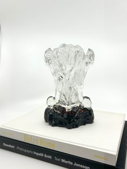 Klare Pertti Santalahti Vase von Humppila aus den 70er Jahren, organische Form mit braun-schwarzem Glasfuß, stehend auf zwei Designbüchern.