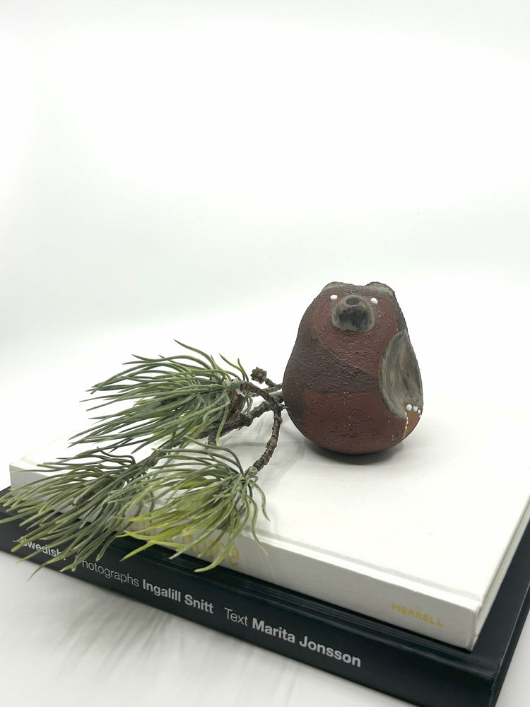 Thomas Hellström Keramikfigur „Bär“ aus den 1980er-Jahren, gefertigt bei Nittsjö, Schweden – rustikale Mid-Century-Dekofigur in Braun auf Bücherstapel mit Tannenzweig inszeniert.