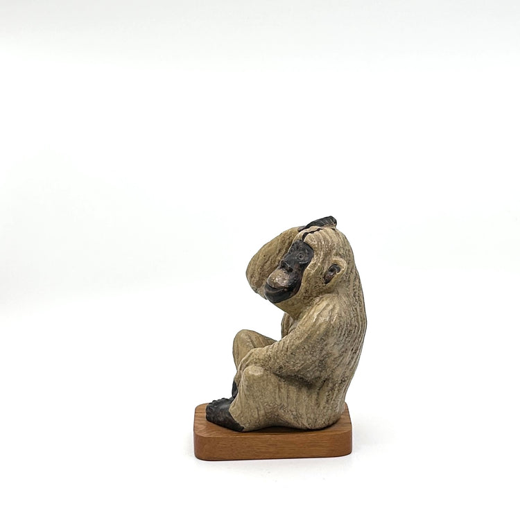 Keramikaffe auf Holzsockel: Seitenansicht Sitzender Affe mit strukturiertem, beigem Fell und dunklen Akzenten, präsentiert auf einem Holzsockel – ikonisches skandinavisches Design der 1960er Jahre