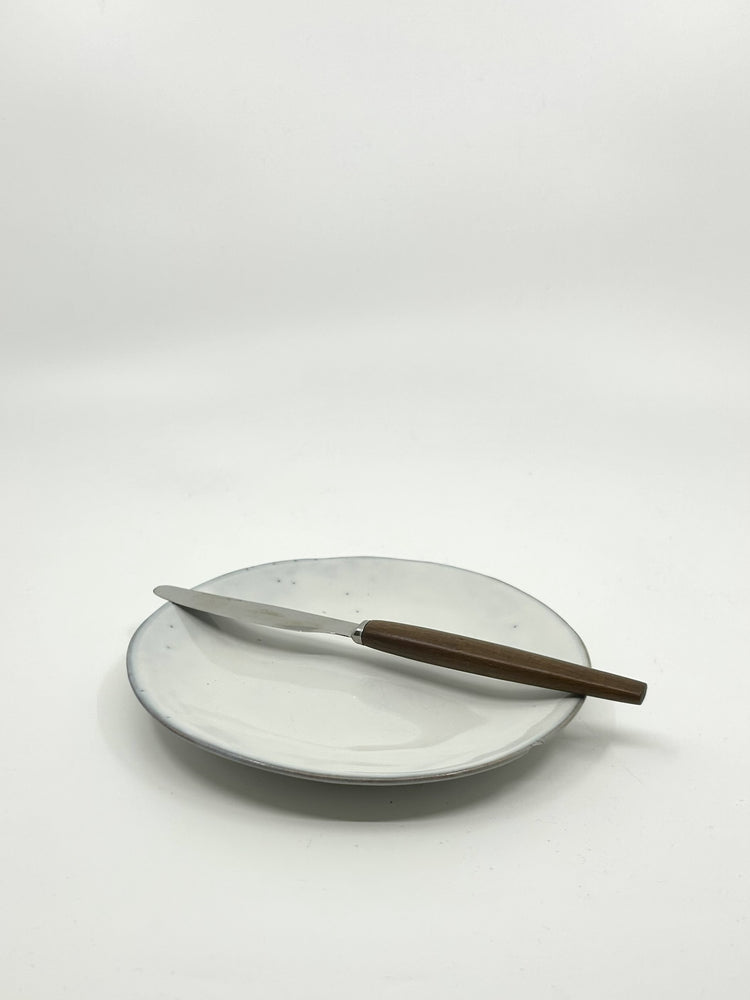 Einzelnes Teakmesser auf Teller – minimalistisches schwedisches Besteckdesign der 1960er Jahre, inspiriert von der Mid Century Ästhetik