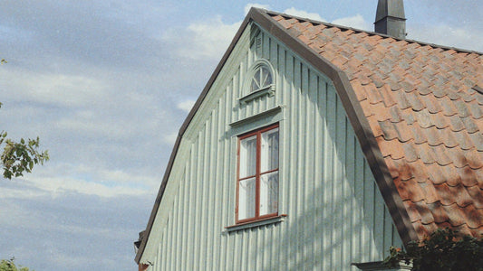Traditionelles Holzhaus in Småland, Schweden – hellgrüne Fassade mit roten Fenstern und typischem Ziegeldach unter sommerlichem Himmel