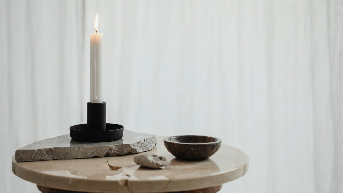 Minimalistischer schwarzer Kerzenhalter mit brennender Kerze auf Marmorplatte, nordisches Stillleben in sanftem Lich