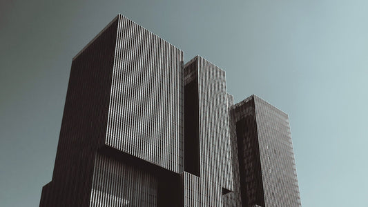 Moderne Hochhaus-Architektur mit klaren Linien und rechteckigen Türmen, aufgenommen im starken Kontrast vor grauem Himmel