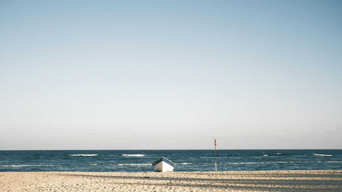 Strand in Dänemark mit beluem Himmel und einem weißen Ruderboot in der Ferne