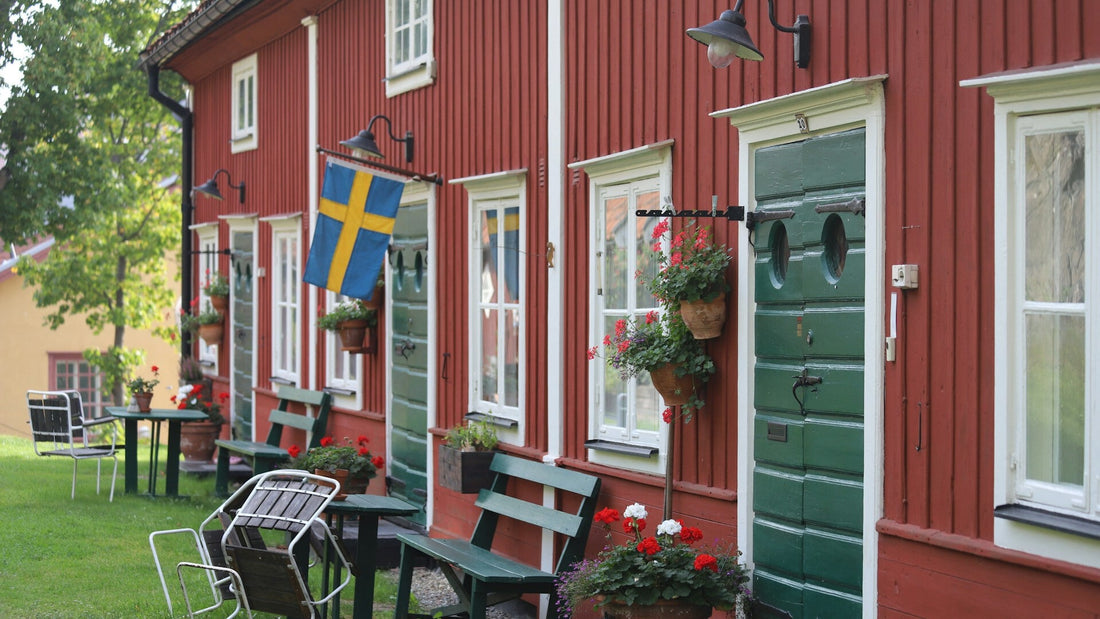 Schwedische Holzhäuser in Falunrot: Traditionelle Häuserzeile mit grünen Bänken, Blumen und schwedischer Flagge – skandinavisches Landleben und Kultur