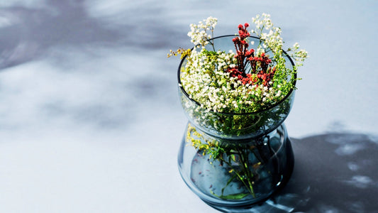 Blaue Glasschale auf zartblauem Grund mit zatren Blüten in weiß und rot gefüllt