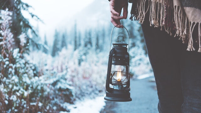 Winterlicher Spaziergang mit brennender Laterne in verschneiter nordischer Landschaft – stimmungsvolle Winteraufnahme im Wald