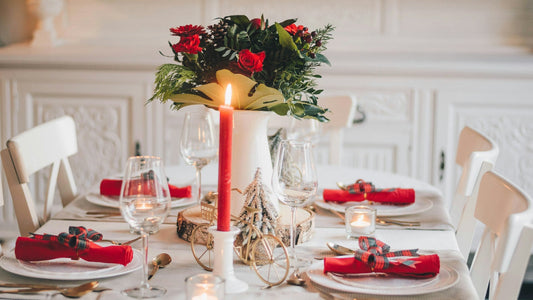 Festlich gedeckte Weihnachtstafel im skandinavischen Stil mit roter Kerze, Blumenarrangement und elegant gefalteten Servietten