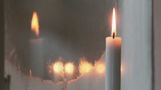 Eine brennende Kerze die sich im gefrostetem Fenster spiegelt