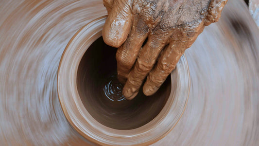 Detailaufnahme einer Hand, die beim Drehen an der Töpferscheibe eine Keramikform gestaltet