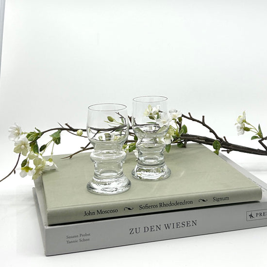 Bertil Vallien 'Gutår' Digestive Glas 5-er Set auf Büchern: Handgefertigte Gläser mit organischen Mustern und goldfarbenen Akzenten, arrangiert mit weißen Blütenzweigen – ikonisches skandinavisches Design der 1970er Jahre