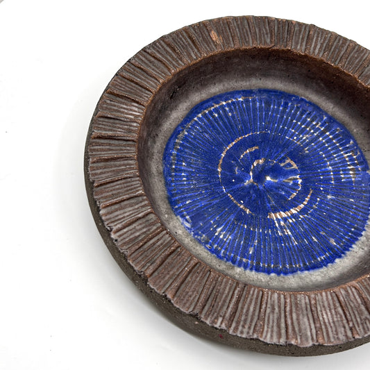 Detailansicht der Thomas Hellström Keramikschale: Nahaufnahme des strukturierten, braunen Randes und des blauen Innenmusters mit weißen Strahlen – schwedische Keramikkunst und dekorative Ästhetik