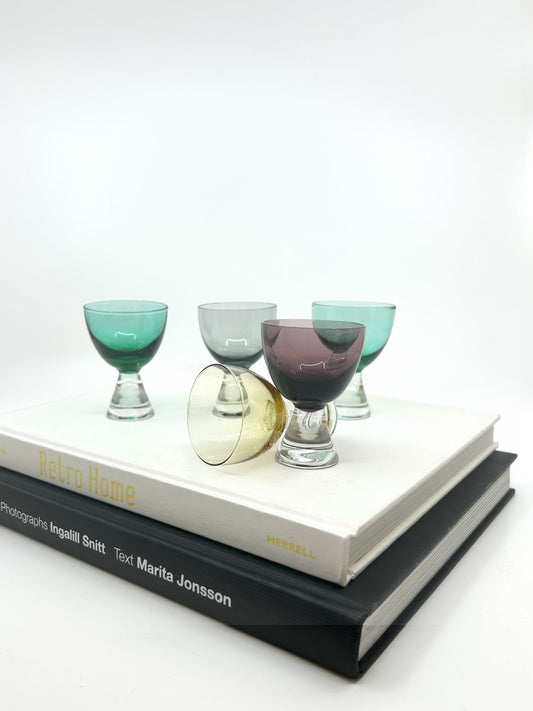 Fünf bunte Mid Century Magnor Digestive Gläser aus Norwegen, 5-teiliges Set in Grün, Grau, Gelb und Lila, arrangiert auf Design-Büchern.