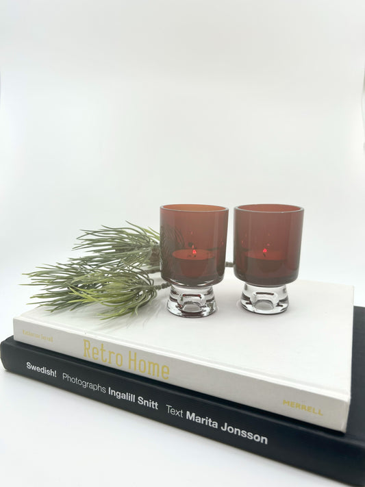 Mid Century Modern Kerzenständer-Set von Tyko Axelsson für Reijmyre – zwei dunkelrote Glas-Kerzenhalter im skandinavischen Design der 60er Jahre, dekorativ auf Retro-Büchern arrangiert.