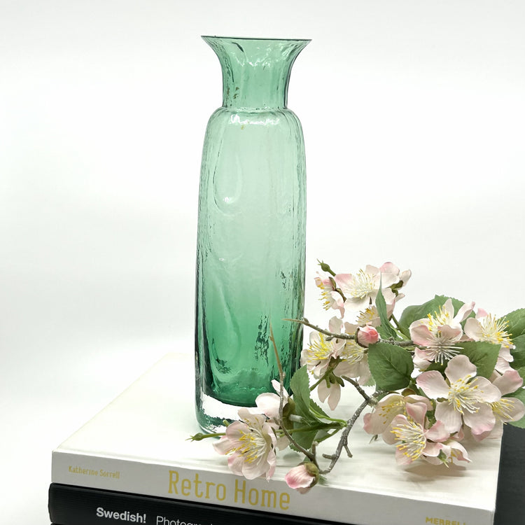 SEA Glasbruk 'Blomknyte' Vase: Handgefertigte Glasvase in Grün mit blumigen Reliefs – hochwertige skandinavische Glaskunst und dekorative Elegan auf Büchern liegend mit Kirschblütenzweig