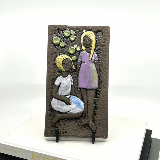 Ninnie Forsgren Wanddeko aus Bromma, Schweden: Keramikrelief mit zwei stilisierten Frauenfiguren in lila und weiß, umgeben von grünen Glasurakzenten – skandinavische Kunsthandwerkstradition und zeitloses Design